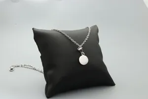Macro view of a silver minimalist round pendant necklace on a black jewelry cushion