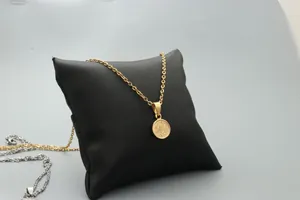 Detail of round gold pendant with botanical engraving on a black jewelry cushion