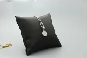 Close-up of silver round pendant necklace with engraved floral pattern on black display