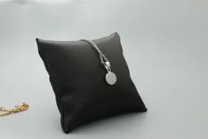 Close-up of a silver circular pendant necklace displayed on a textured black cushion
