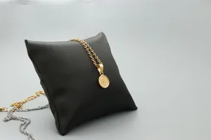 Macro detail of round gold pendant with embossed floral pattern on black jewelry cushion