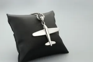 Primer plano de un colgante de avión plateado sobre cojín negro con cadena de bolas