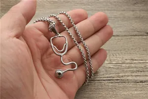 Detailed view of silver stethoscope pendant necklace held by hand over a wooden table