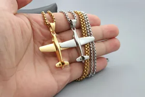 Detalle de dos collares con colgante de avión sostenidos a mano en metal pulido oro y plata