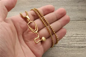Detail of a golden stethoscope pendant necklace on a box chain held in hand