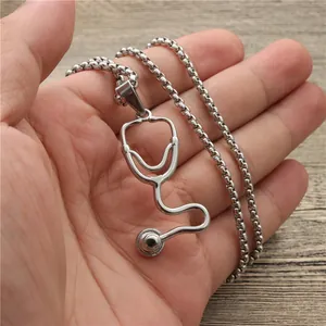 Silver stethoscope pendant necklace with box chain held in hand over a wooden background