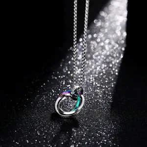 Collier pendentif trois anneaux en acier titane argent, gris et arc-en-ciel sur sable noir