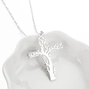 Collier avec pendentif croix ajourée en acier argenté posé sur un plateau en céramique