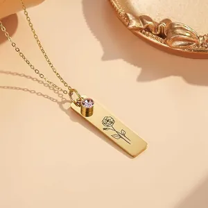Gold rectangular pendant necklace with engraved rose and purple gemstone on warm background
