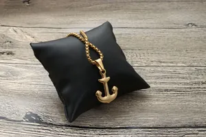 Détail d'un pendentif ancre dorée avec chaîne gourmette sur un support en cuir noir