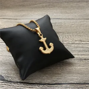 Collier avec pendentif ancre dorée et chaîne box posé sur un coussin en cuir noir chic