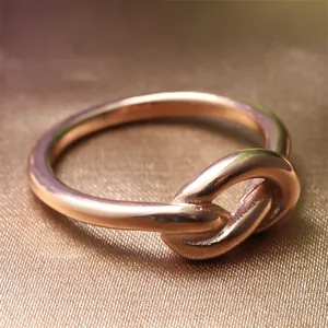 Dettaglio macro di un anello a nodo in oro rosa lucido su elegante tessuto marrone