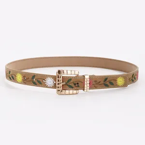 Detail of floral embroidery on brown suede belt with vintage gold patterned buckle