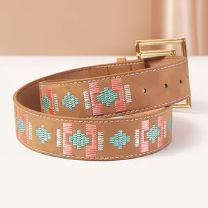 Macro detail of brown leather belt featuring geometric embroidery and golden buckle