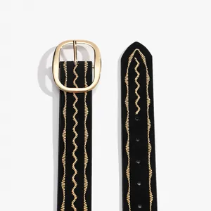 Close-up of black leather belt with golden wave embroidery and oval buckle detail
