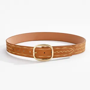 Détail d'une ceinture en cuir marron avec boucle dorée et surpiqûres blanches ondulées