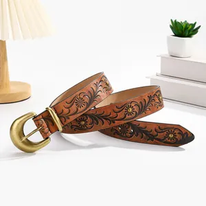 Vintage caramel brown leather belt with black floral embossing and brass buckle on white desk