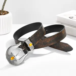 Vintage western belt with embossed silver buckle and yellow gemstone on white surface