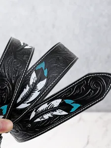Détail d'une ceinture western en cuir noir avec fleurs gaufrées et plumes peintes en bleu