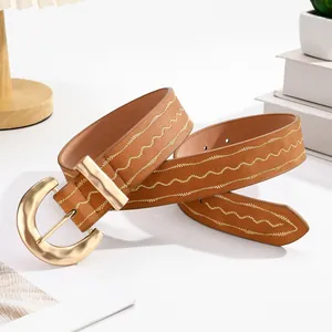 Détail d'une ceinture marron avec broderie dorée ondulée et boucle ardillon texturée