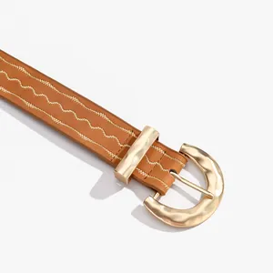 Détail d'une ceinture en cuir marron avec broderie dorée ondulée et boucle en métal poli