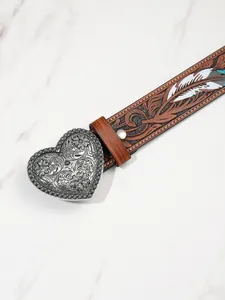 Dettaglio di cintura in pelle marrone vintage con rilievo floreale e fibbia a cuore in metallo