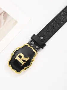Detail van zwarte lederen riem met reliëf en een grote gouden letter R gesp