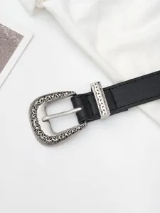 Macro shot of black pebbled leather belt with ornate silver western buckle and floral carvings