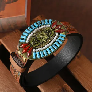 Detail of western cowboy belt buckle with turquoise beads and red gems on embossed leather