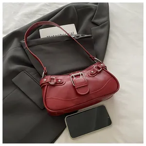 Detail view of red PU leather underarm bag with silver buckles and smartphone for scale