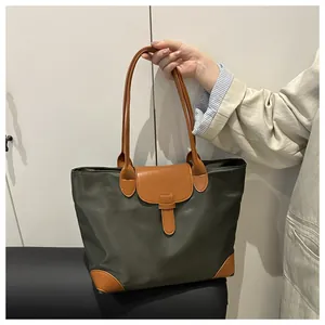 Detail of green nylon tote bag with brown leather contrast handles and buckled flap