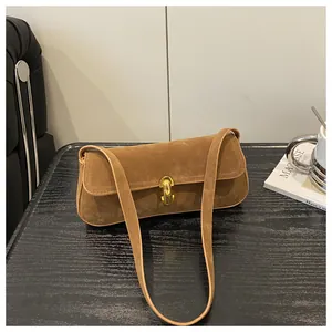 Detail of a brown suede underarm bag with a gold oval twist lock on a wooden table