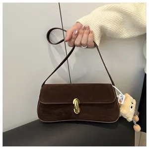 Detail of dark brown faux suede underarm bag with gold lock and plush pendant accessory
