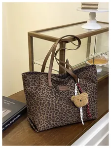 Dettaglio della borsa tote leopardata con manici in pelle marrone e ciondolo a orsetto