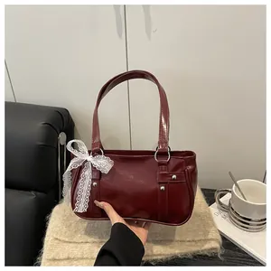 Close-up of deep red Boston bag with silver rivets and white lace bow on scarf