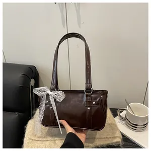 Detail of dark brown glossy patent leather bag with white lace bow and silver rivets