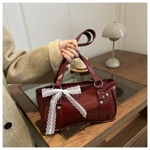 Detail of burgundy glossy underarm bag with large white lace bow and silver rivets