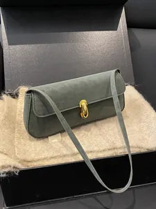 Dunkelgrüne Wildleder-Baguette-Tasche mit Goldverschluss auf weichem Hintergrund