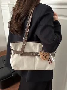 Dettaglio borsa tote in tela color crema con cinturini in ecopelle marrone e ciondolo orso