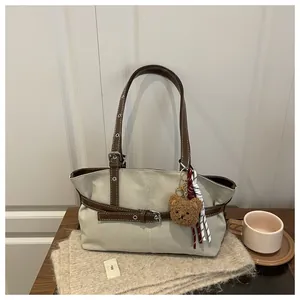 Dettaglio della borsa tote in tela con cinturini in pelle marrone e ciondolo orso