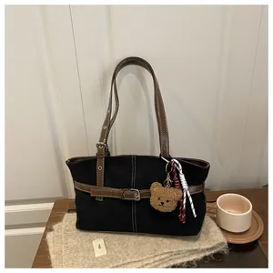 Dettaglio della borsa tote in tela nera con cinturini in pelle marrone e ciondolo a orsetto