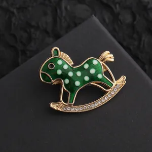 Close-up of a green enamel rocking horse brooch with gold accents and sparkling rhinestones