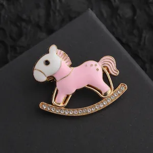 Close-up of golden rocking horse brooch with pink enamel and sparkling rhinestones