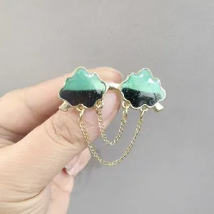 Close-up of cloud enamel brooch with green and black tones and double gold chain