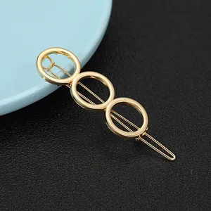 Close-up of golden geometric hair clip with three hollow rings on black leather background