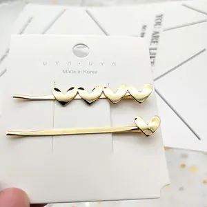 Dettaglio di un set di due fermagli per capelli dorati a cuore su cartoncino bianco