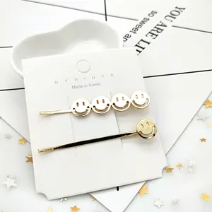 Dettaglio di due fermagli per capelli dorati con smile su carta con paillettes