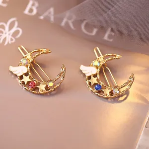 Détail de barrettes lune dorées avec cristaux colorés et petites ailes d'ange blanches