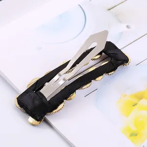 Elegant fabric hair clip with gold accents and pearls on a clean minimalist background