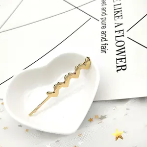 Dettaglio di un fermaglio per capelli a cuore dorato su un piatto in ceramica bianca
